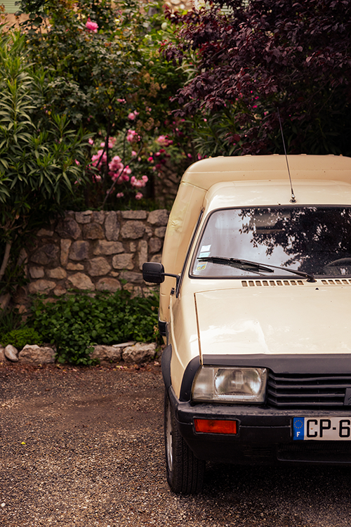 An old Citroën model parked by a wall with lush greenery