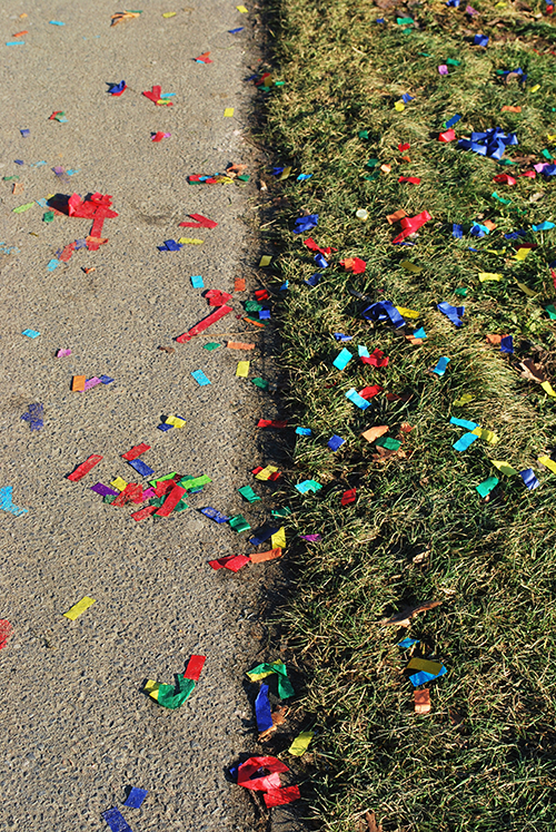 Confetti scattered at the edge of an asphalt path and lawn