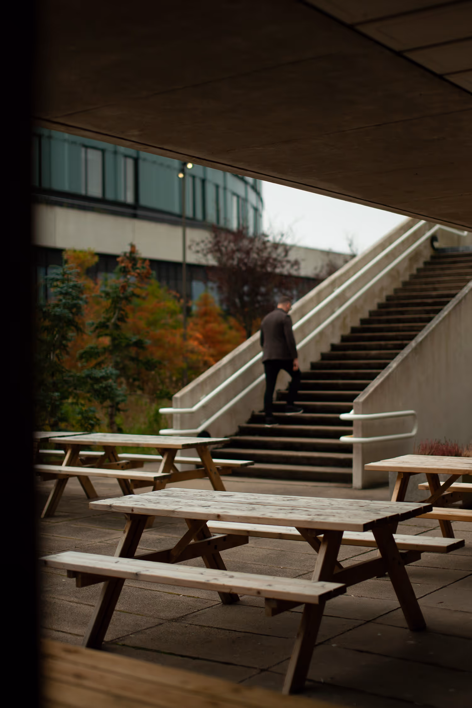 A figure ascends a concrete staircase at Herlev Hospital in Copenhagen, framed by a concrete overhang, emphasizing brutalist architecture and strong leading lines.
