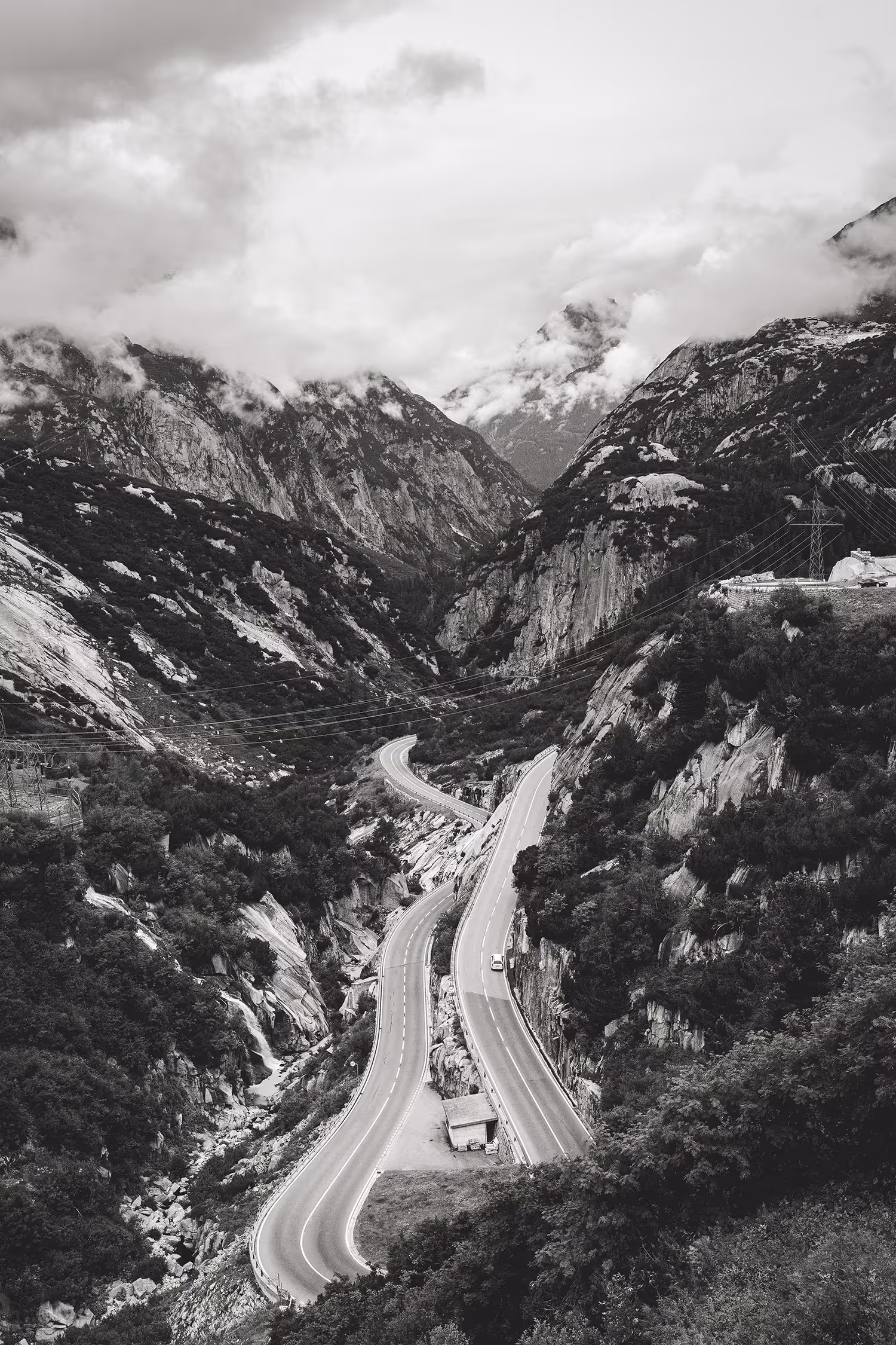 Monochrome fine art landscape of the winding alpine road near Oberhasli power plant in the Swiss Alps, featuring high contrast, dramatic clouds, and leading lines.