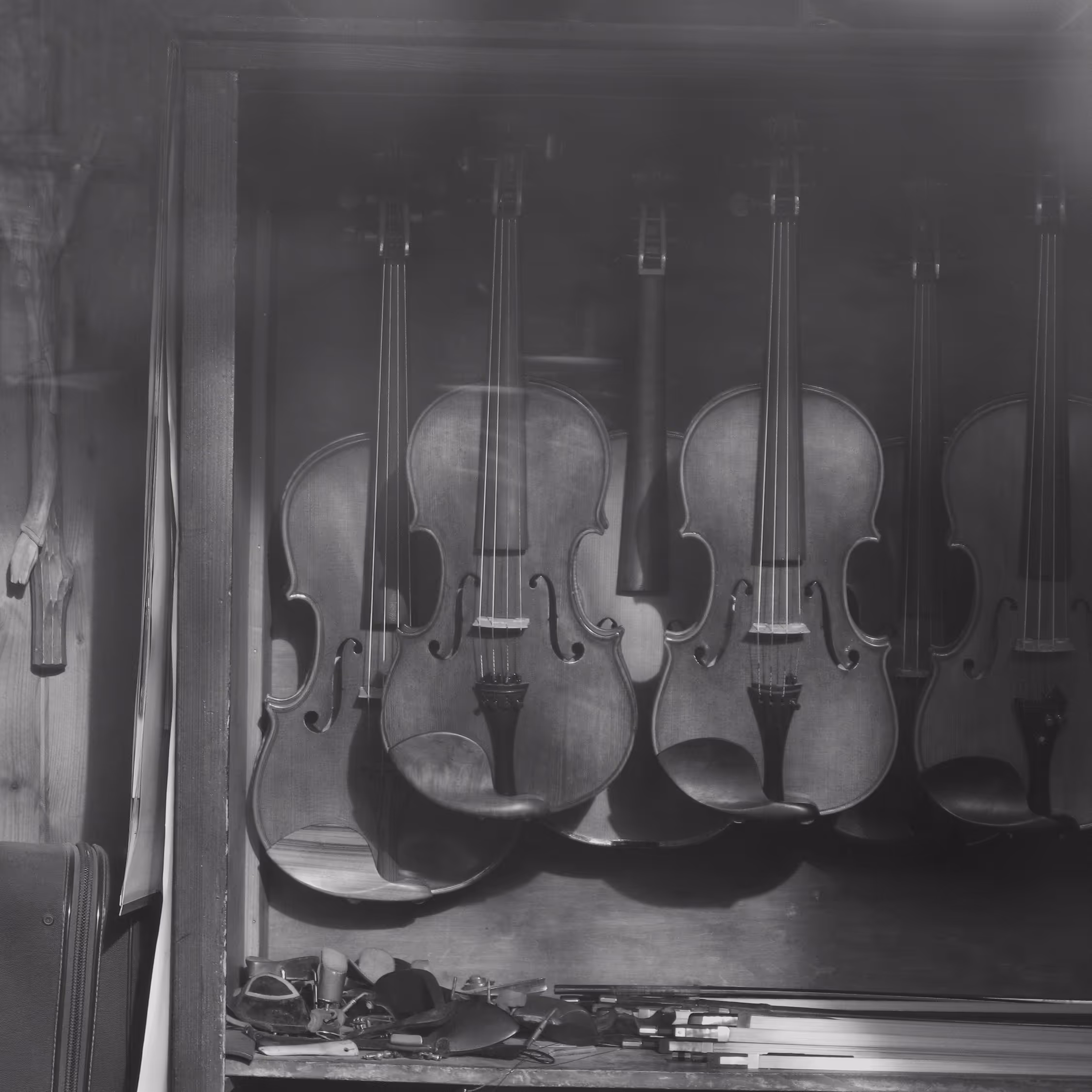 Atmospheric black and white fine art photography of a luthier's window display in a Krakow antique shop, featuring a row of vintage violins and bows evoking a nostalgic, musical heritage.