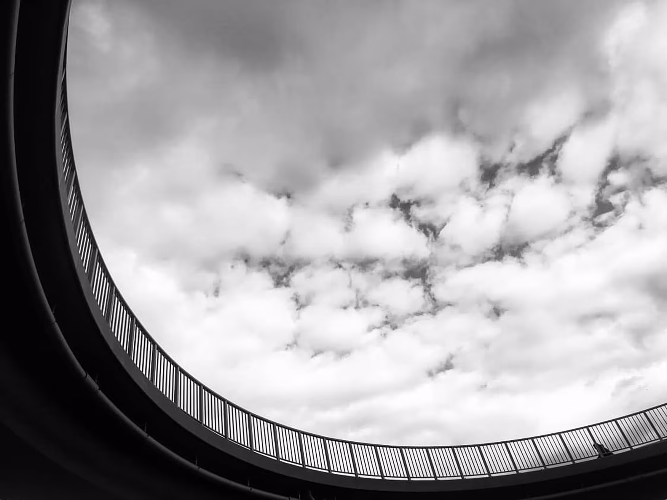 Abstract black and white architectural photography in Krakow, featuring a low-angle shot of a dramatic cloudy sky framed by the geometric curve of a modern structure.